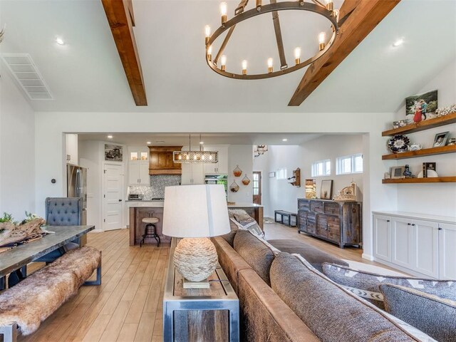 living area featuring lofted ceiling with beams, light wood finished floors, a chandelier, and visible vents