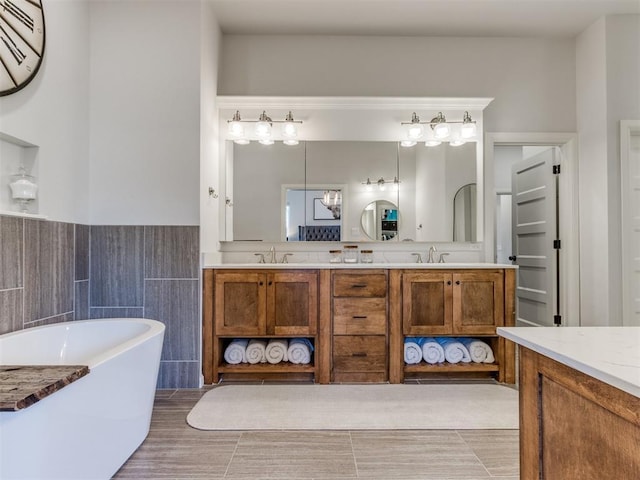 full bathroom with a freestanding bath, double vanity, tile walls, and a sink