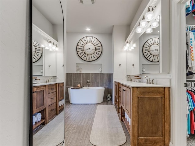 bathroom featuring a walk in closet, two vanities, a soaking tub, and a sink