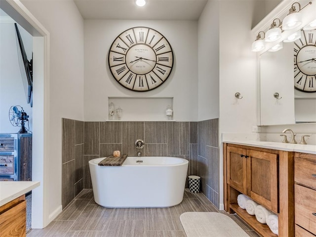 bathroom featuring tile walls, a soaking tub, a wainscoted wall, and vanity