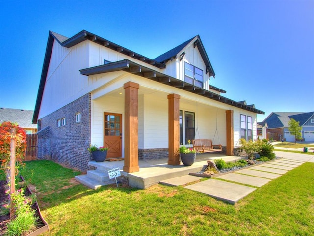 back of house featuring a porch, fence, brick siding, a lawn, and board and batten siding