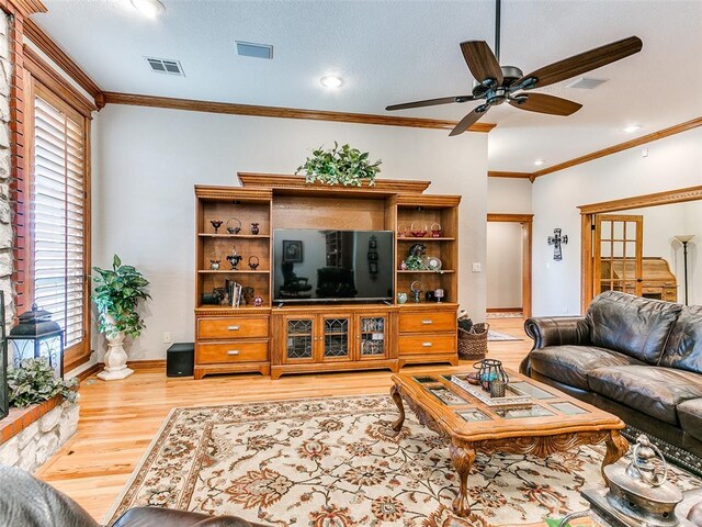 living area featuring a ceiling fan, visible vents, ornamental molding, and wood finished floors