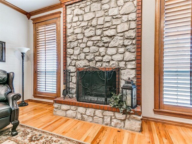 interior details with crown molding, baseboards, a stone fireplace, and wood finished floors