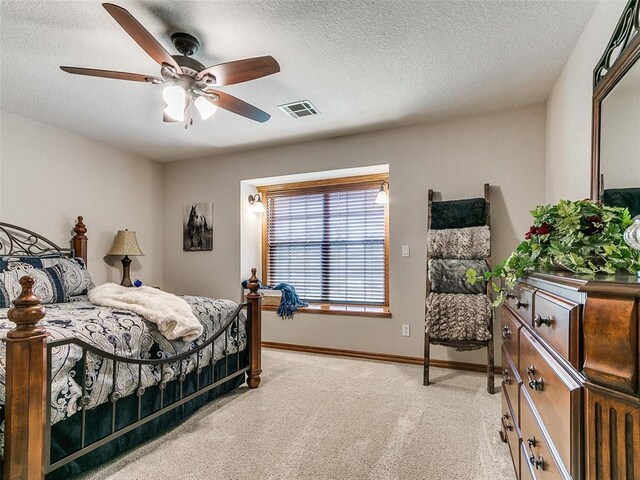 bedroom with ceiling fan, a textured ceiling, visible vents, baseboards, and light carpet