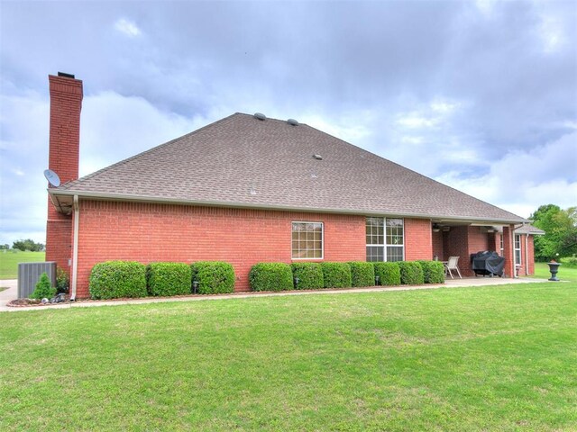 back of property featuring brick siding, a chimney, a patio area, central air condition unit, and a lawn