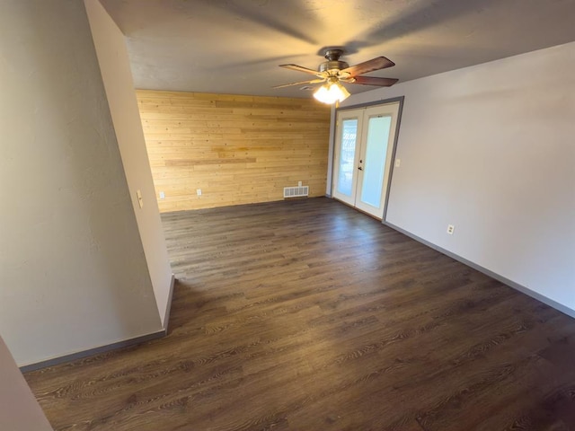 empty room featuring wood walls, visible vents, french doors, dark wood-type flooring, and ceiling fan