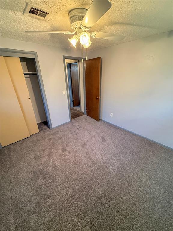 unfurnished bedroom featuring carpet floors, a ceiling fan, a textured ceiling, and visible vents