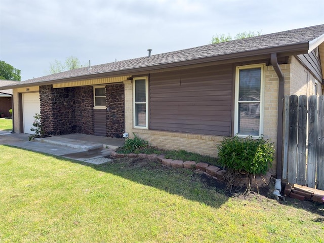 exterior space with a lawn, a shingled roof, an attached garage, fence, and brick siding