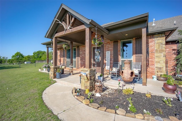 view of front of property with fence, a shingled roof, brick siding, a porch, and a front yard