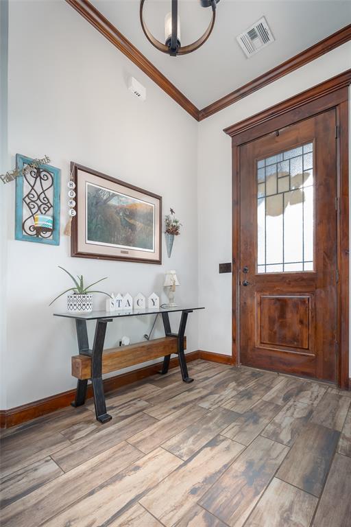 entryway featuring baseboards, ornamental molding, light wood-style flooring, and visible vents