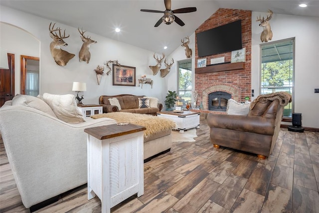 living area with ceiling fan, a brick fireplace, arched walkways, wood finished floors, and lofted ceiling