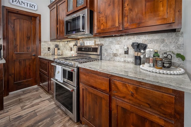 kitchen with backsplash, appliances with stainless steel finishes, wood finished floors, and light stone counters