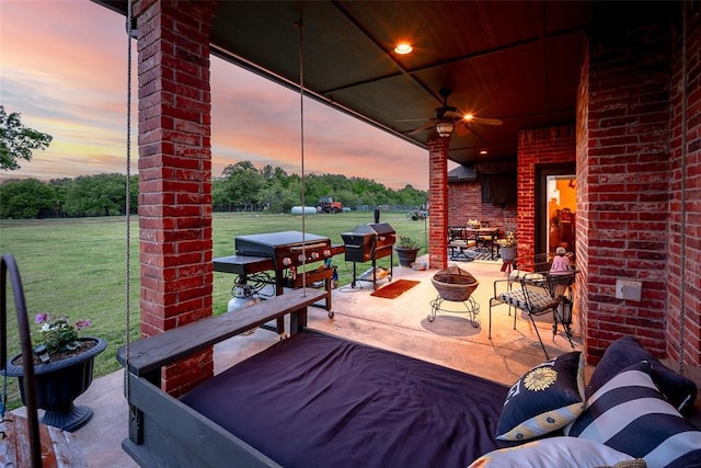 patio terrace at dusk with a lawn, ceiling fan, and a fire pit