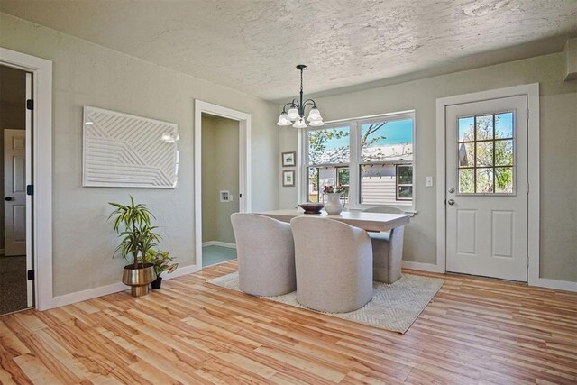 dining room with baseboards, an inviting chandelier, a textured ceiling, and light wood-style flooring