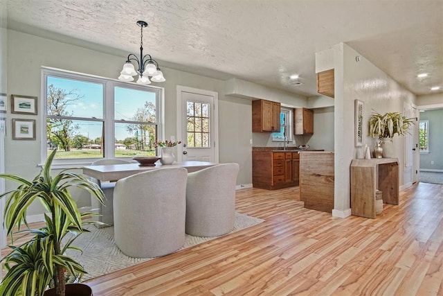 dining area with baseboards, a chandelier, light wood-style floors, and a textured ceiling