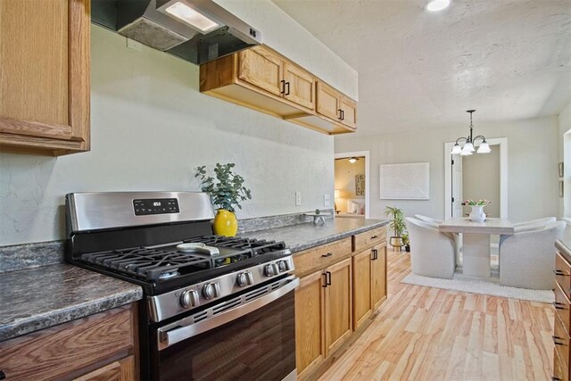 kitchen with stainless steel gas range, light wood-type flooring, dark countertops, extractor fan, and an inviting chandelier
