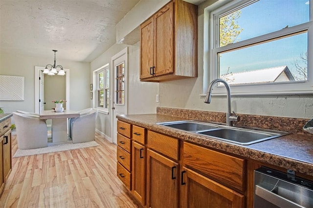 kitchen with brown cabinets, dishwasher, a sink, light wood-style floors, and a notable chandelier