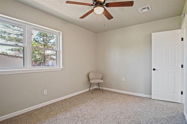 spare room with light colored carpet, baseboards, a ceiling fan, and visible vents
