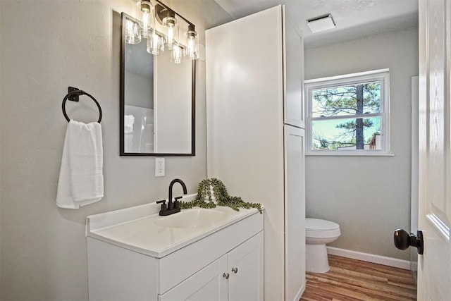 bathroom with baseboards, wood finished floors, toilet, and vanity