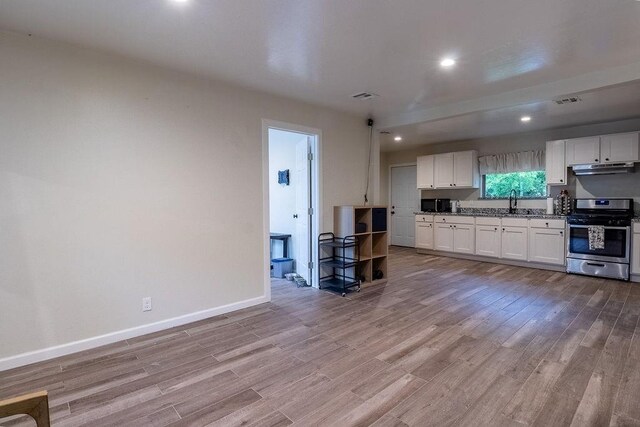 kitchen featuring stainless steel range with gas stovetop, light wood-style flooring, under cabinet range hood, and white cabinetry