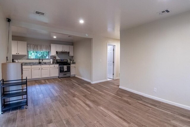kitchen with visible vents, gas range, baseboards, light wood-style floors, and white cabinetry