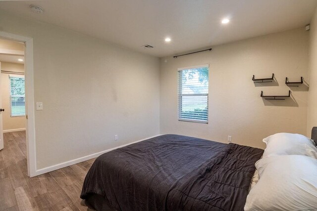 bedroom featuring baseboards, visible vents, multiple windows, and wood finished floors