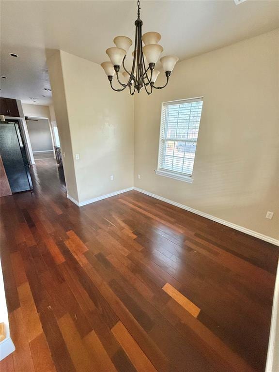 unfurnished dining area featuring baseboards, an inviting chandelier, and dark wood-style flooring