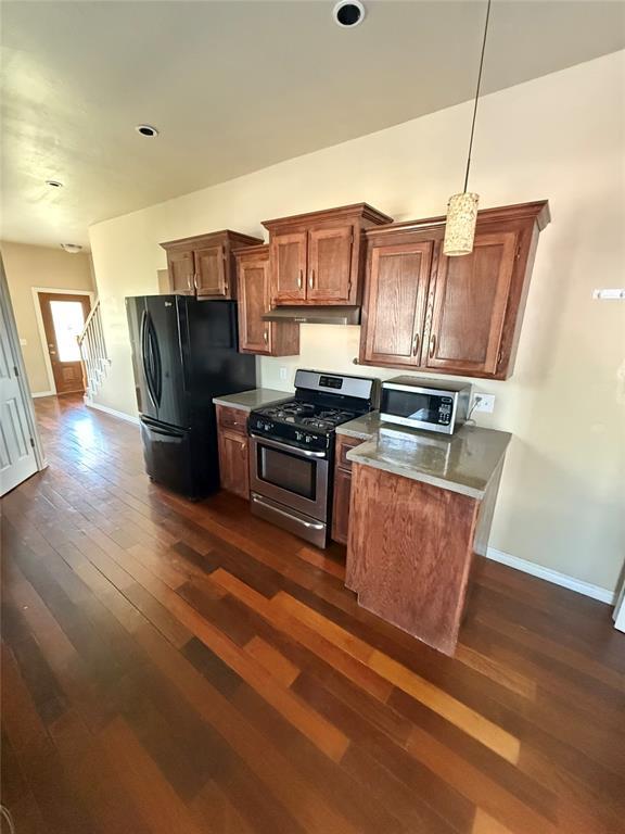 kitchen featuring dark wood finished floors, baseboards, under cabinet range hood, and stainless steel appliances