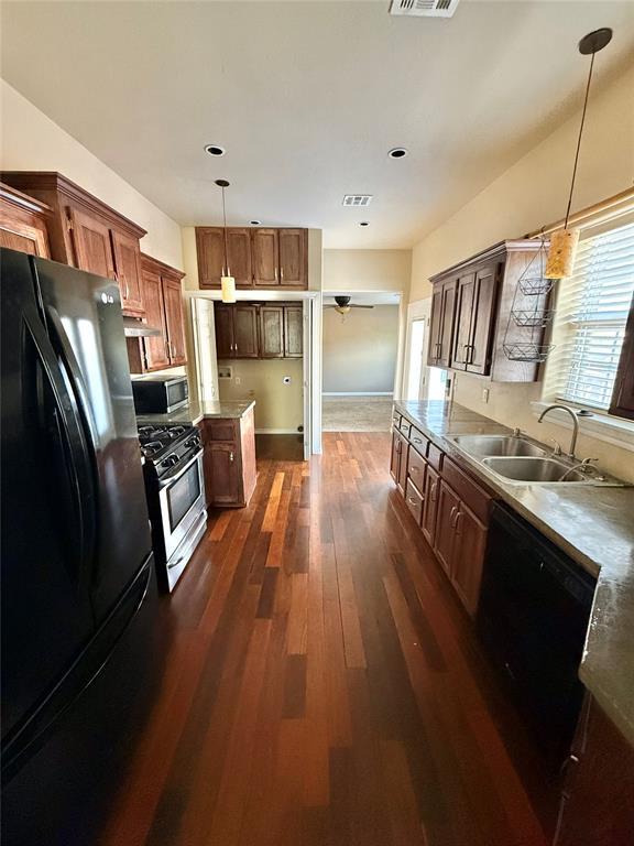 kitchen featuring wall chimney range hood, a sink, black appliances, pendant lighting, and dark wood-type flooring