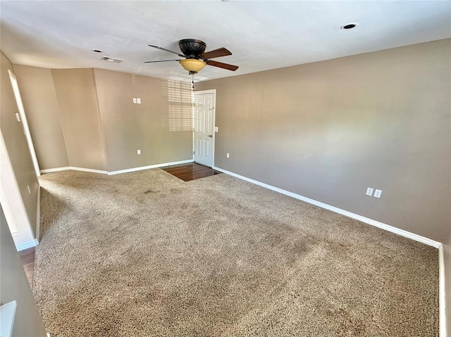 empty room with carpet floors, a ceiling fan, visible vents, and baseboards
