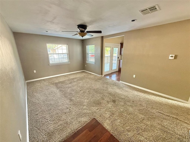 empty room with dark carpet, visible vents, baseboards, and ceiling fan