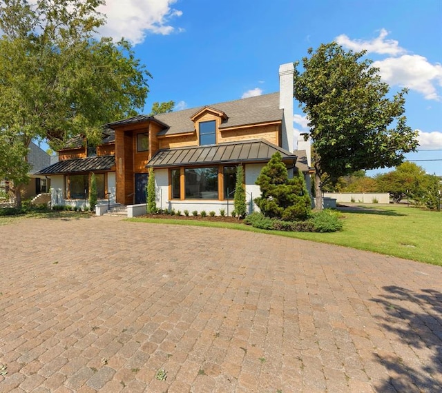 view of front of house featuring a chimney, metal roof, a shingled roof, a front yard, and a standing seam roof