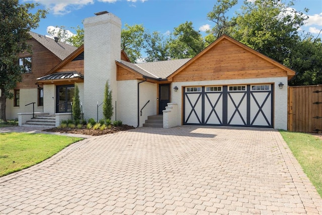 view of front facade with a chimney, decorative driveway, brick siding, a front yard, and a garage