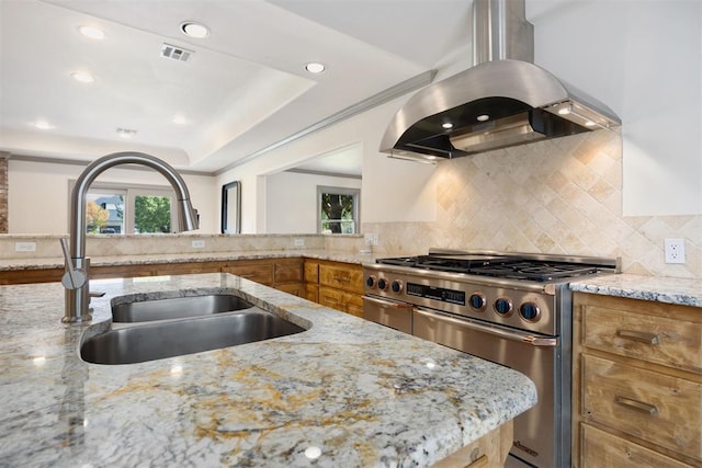 kitchen featuring a sink, high end stainless steel range oven, visible vents, island range hood, and brown cabinetry