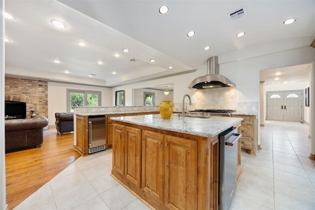 kitchen featuring a sink, an island with sink, light tile patterned floors, island exhaust hood, and visible vents