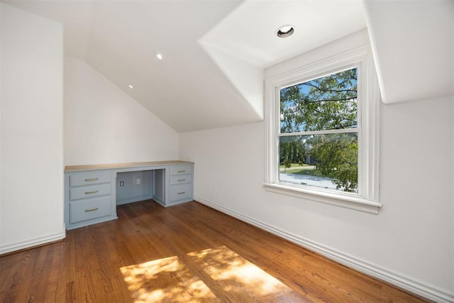bonus room with baseboards, vaulted ceiling, wood finished floors, and built in desk