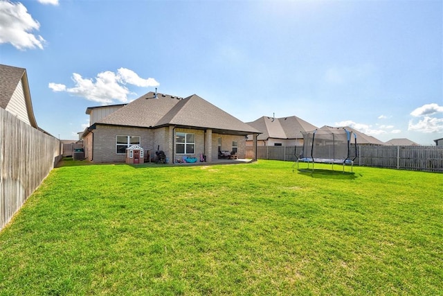 13513 NW 1st St, Yukon, OK 73099 - rear view of property featuring a trampoline, brick siding, a fenced backyard, a lawn, and a patio