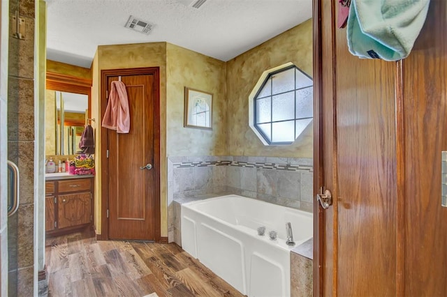 bathroom featuring wood finished floors, visible vents, vanity, a bath, and a textured ceiling