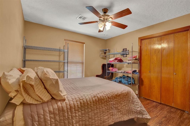 bedroom with a ceiling fan, a textured ceiling, wood finished floors, a closet, and visible vents