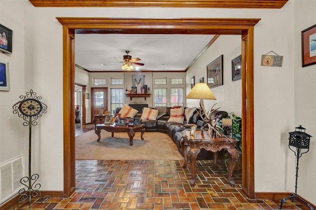 living room with baseboards, visible vents, ceiling fan, crown molding, and brick floor