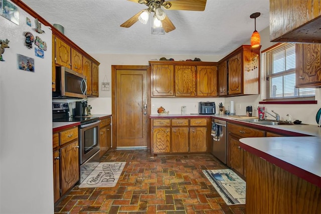 kitchen featuring a textured ceiling, brick floor, a sink, brown cabinets, and stainless steel appliances