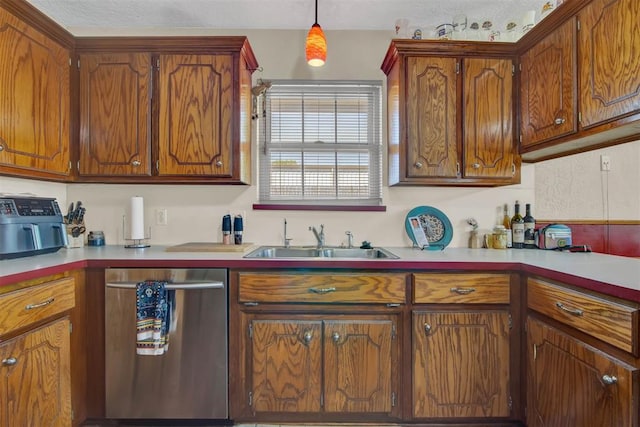 kitchen with stainless steel dishwasher, a sink, pendant lighting, brown cabinetry, and light countertops