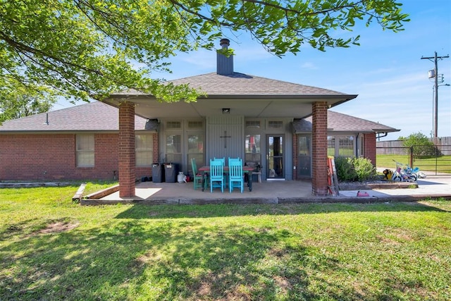 back of house with a chimney, brick siding, a patio, and a lawn