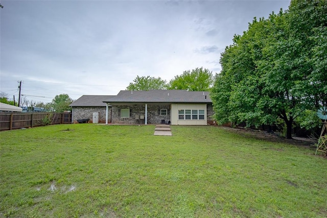 back of property featuring a yard, fence, and stone siding