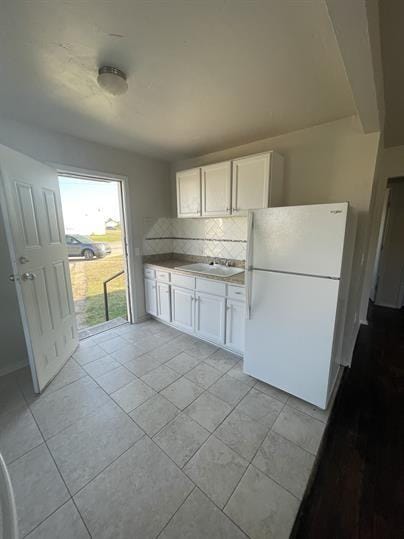 kitchen featuring freestanding refrigerator, white cabinets, tasteful backsplash, a sink, and light tile patterned floors