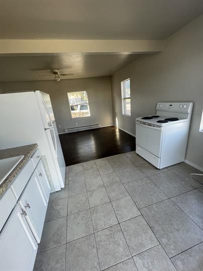 kitchen featuring light tile patterned floors, a baseboard radiator, plenty of natural light, and white appliances
