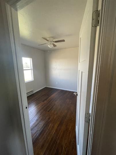 spare room with a baseboard heating unit, ceiling fan, dark wood finished floors, and baseboards