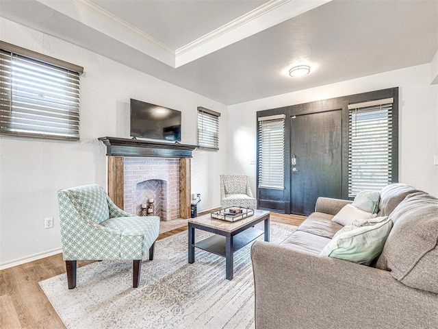 living room featuring baseboards, wood finished floors, crown molding, and a brick fireplace