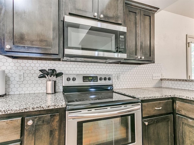 kitchen featuring dark brown cabinetry, stainless steel appliances, light stone countertops, and backsplash