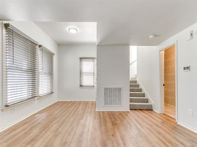 unfurnished living room with baseboards, visible vents, stairway, and light wood-style flooring